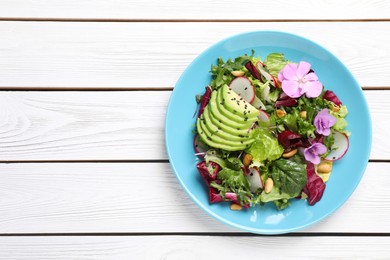 Photo of Fresh spring salad with flowers in plate on white wooden table, top view