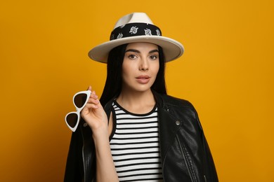 Fashionable young woman in stylish outfit with bandana on orange background