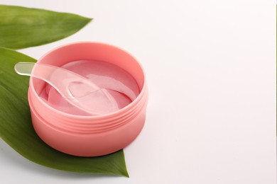 Jar of under eye patches with spoon and green leaves on white background, closeup with space for text. Cosmetic product