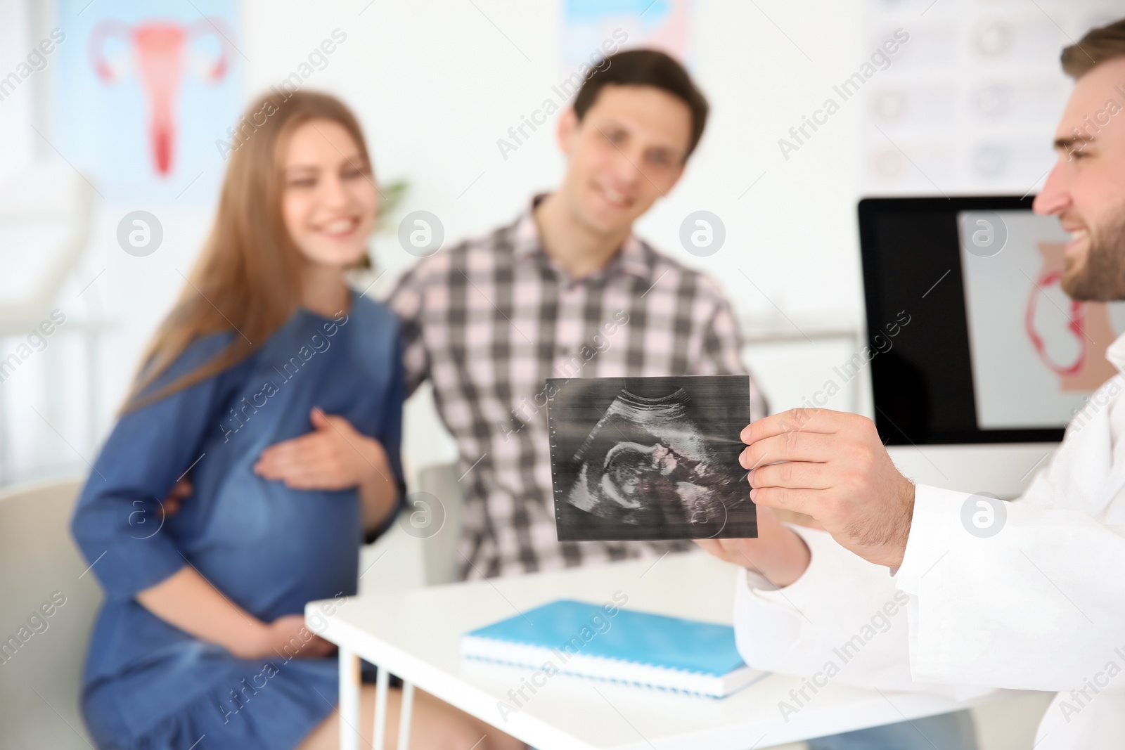 Photo of Gynecology consultation. Doctor showing ultrasound of baby to future parents in clinic