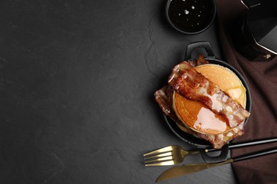 Delicious pancakes with maple syrup and fried bacon on black table, flat lay. Space for text