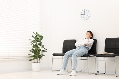 Photo of Tired woman sitting on chair and waiting for appointment indoors