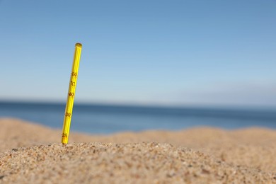 Weather thermometer in sand near sea, space for text