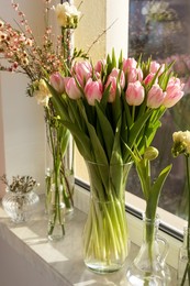 Many different spring flowers and branches with leaves on windowsill indoors