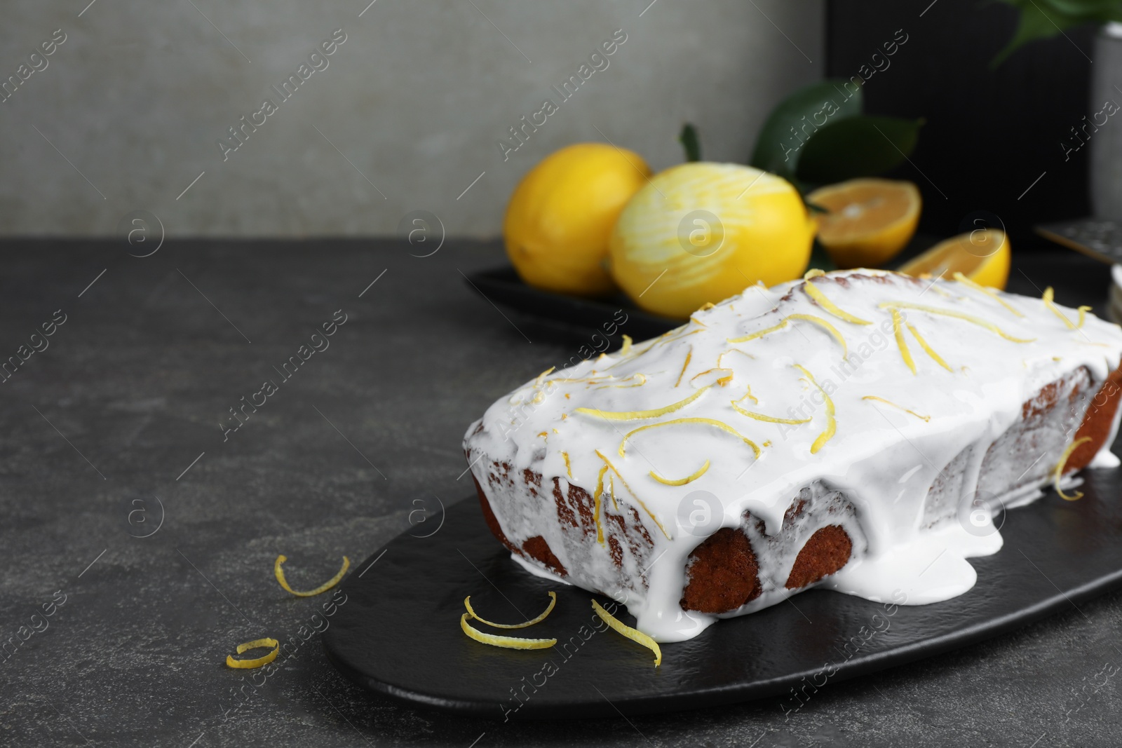 Photo of Tasty lemon cake with glaze and citrus fruits on gray table, closeup. Space for text