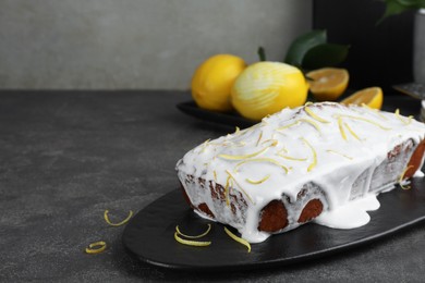 Photo of Tasty lemon cake with glaze and citrus fruits on gray table, closeup. Space for text