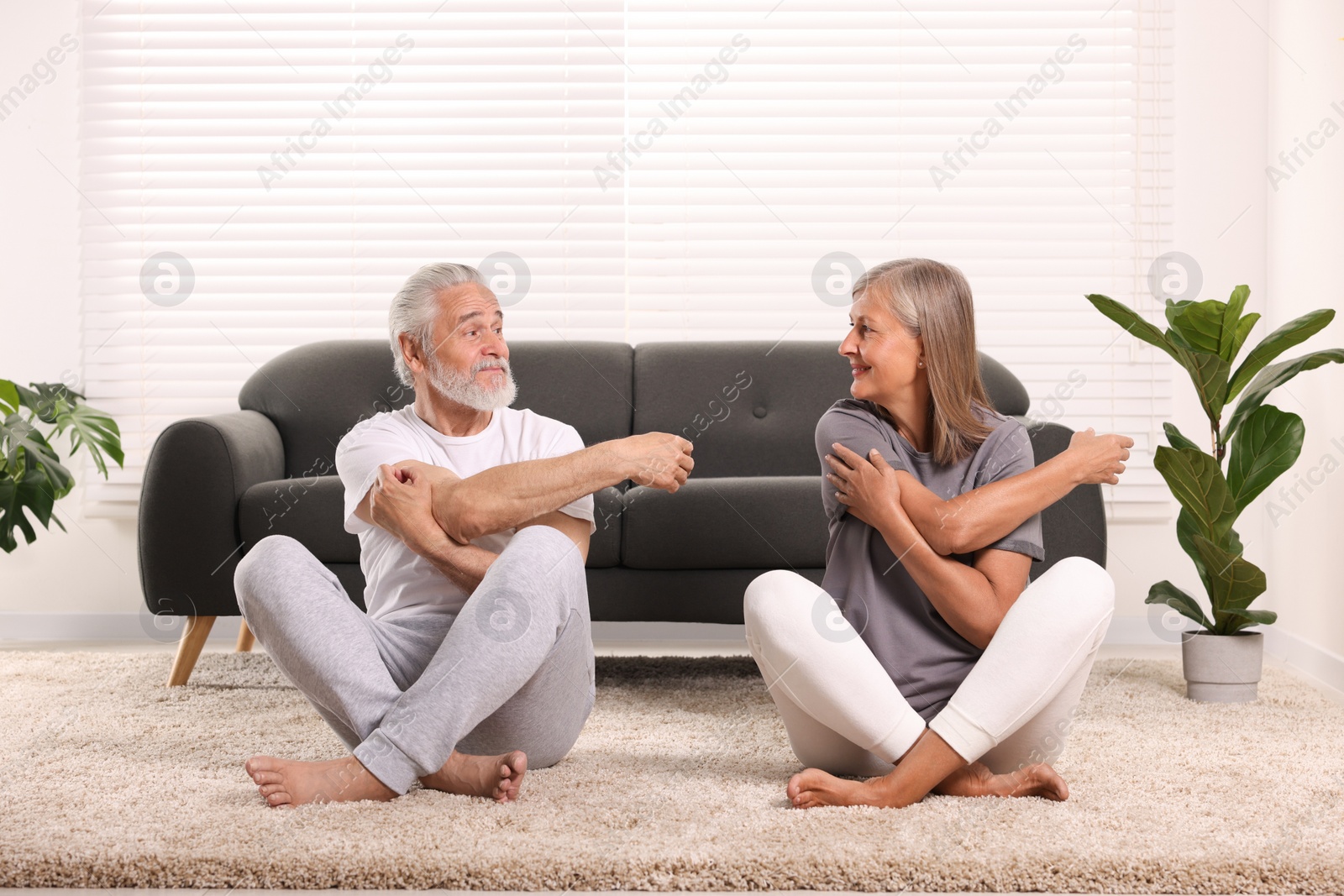 Photo of Senior couple practicing yoga on carpet at home. Healthy lifestyle