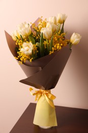 Bouquet with beautiful spring flowers on wooden table near beige wall