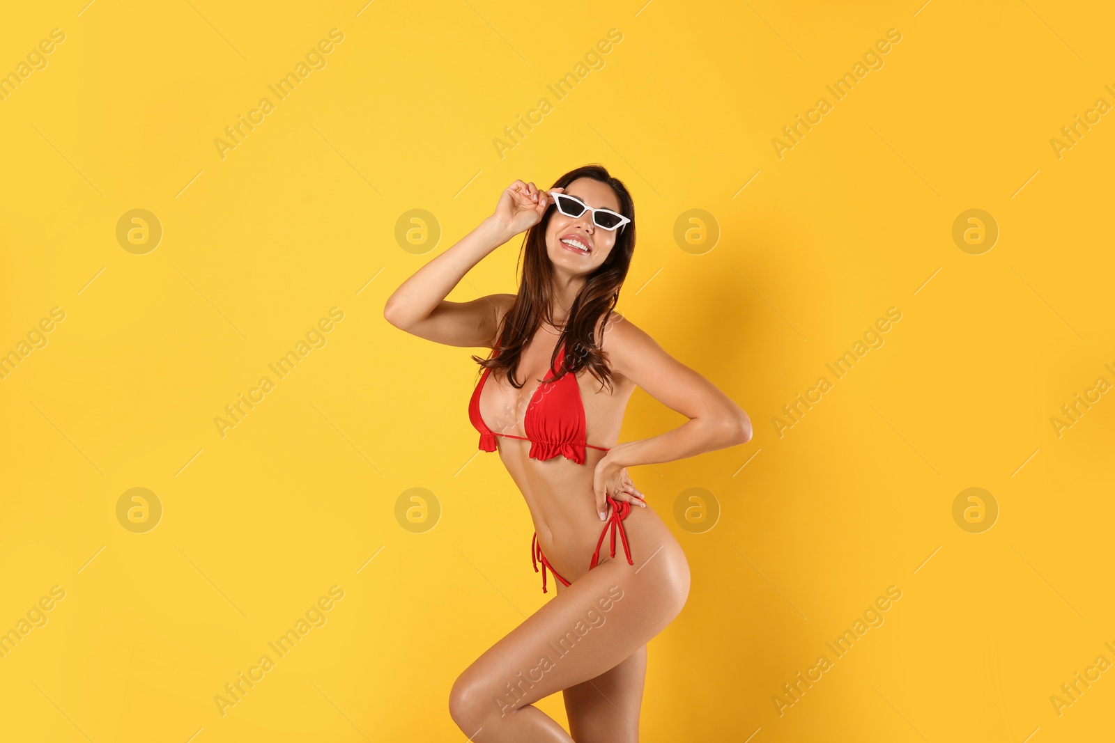 Photo of Beautiful woman in stylish bikini and sunglasses on yellow background