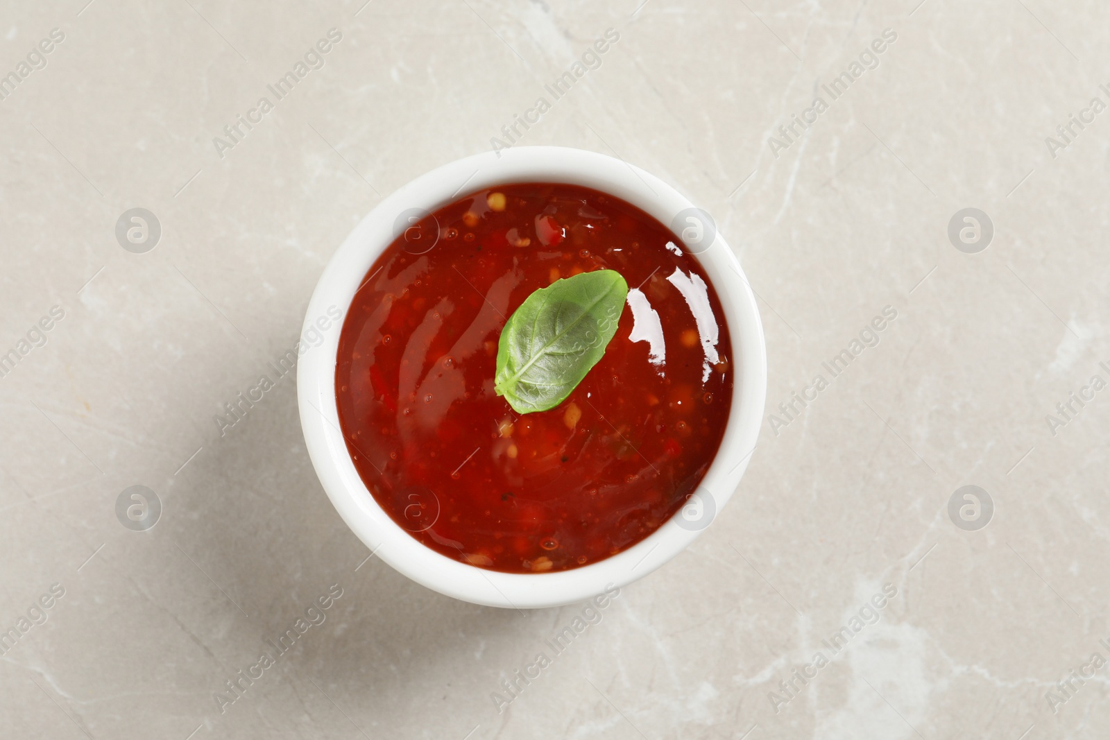 Photo of Spicy chili sauce with basil on light table, top view