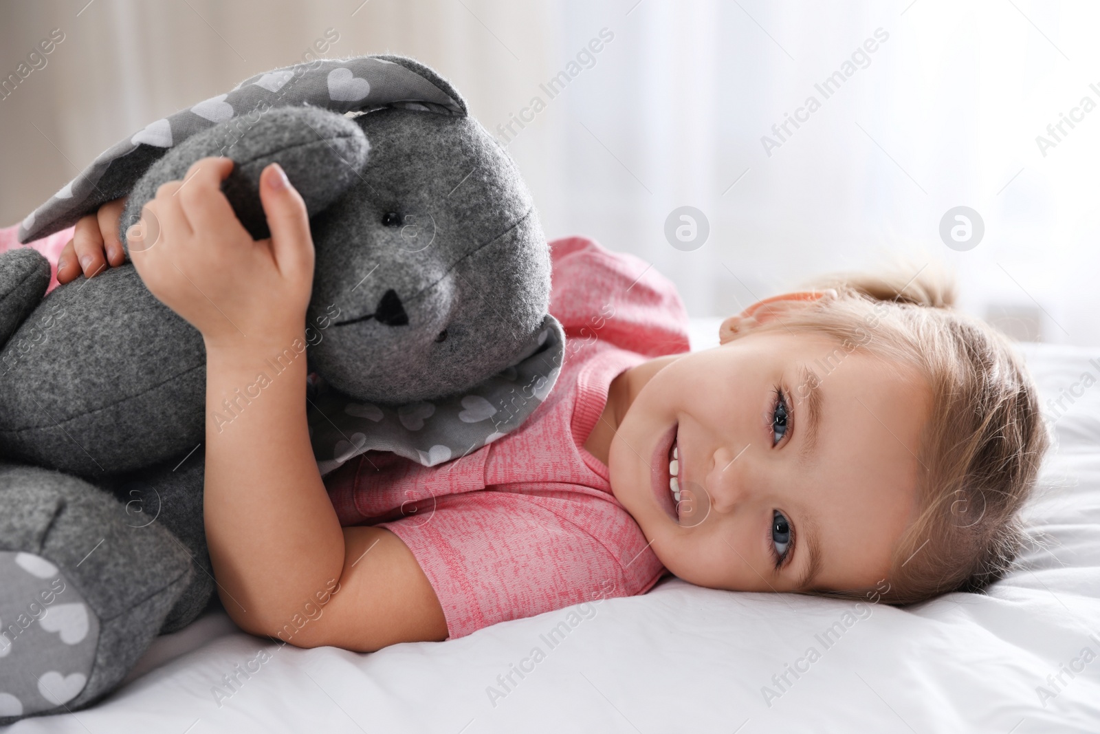 Photo of Cute little girl with toy bunny on bed at home