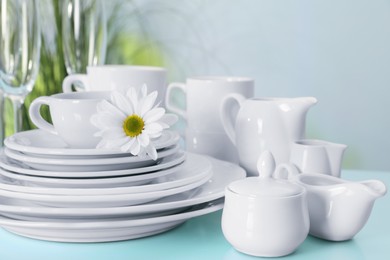 Photo of Set of clean dishware and flower on light blue table, closeup