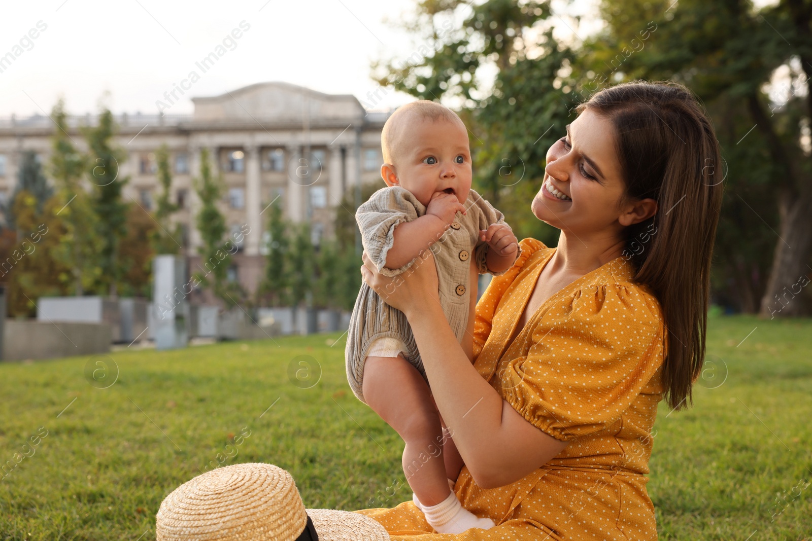 Photo of Happy mother with adorable baby sitting on green grass in park, space for text