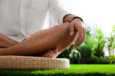 Young man meditating on straw cushion outdoors, closeup