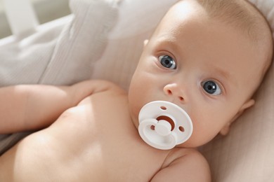 Photo of Cute little baby with pacifier lying in crib