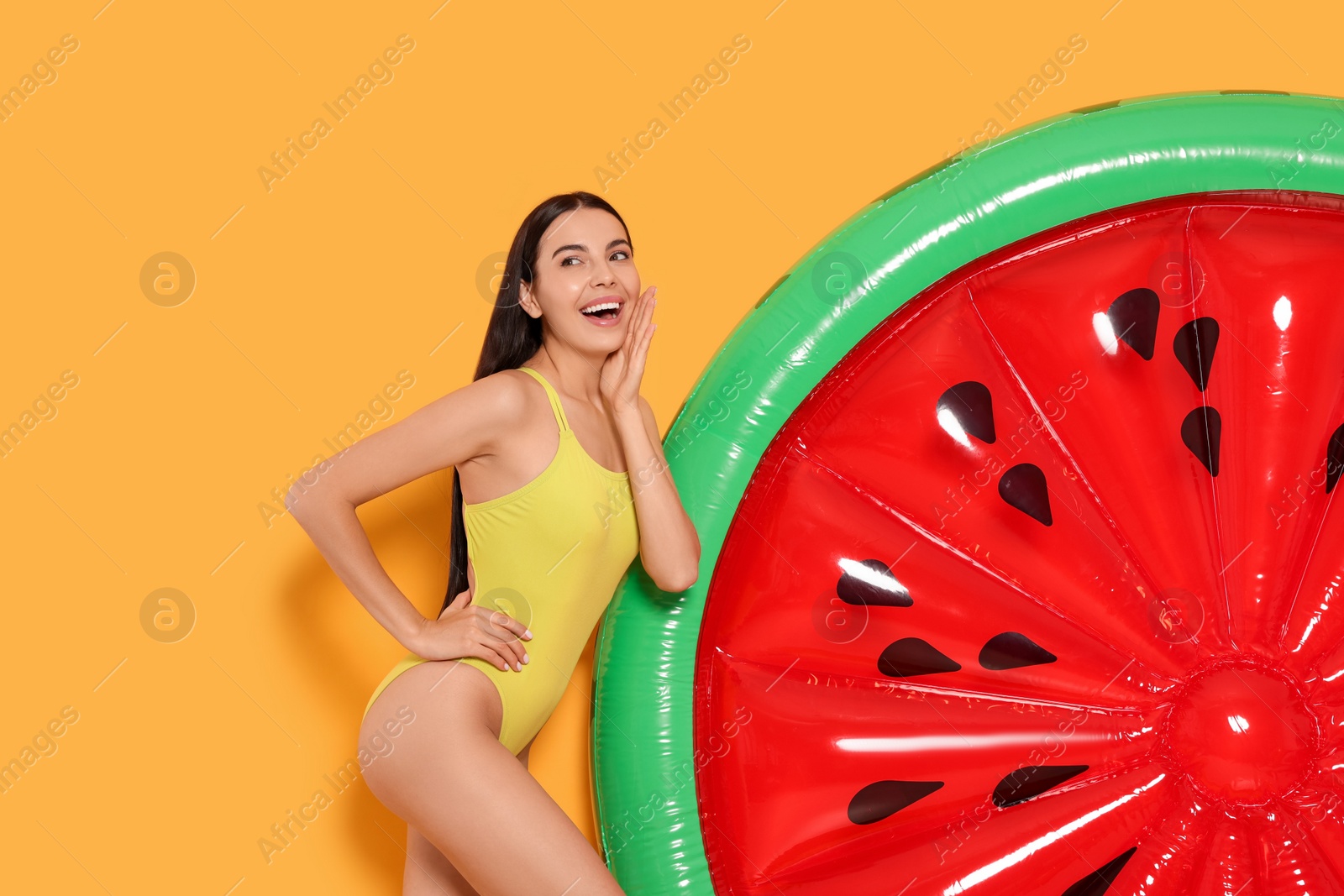 Photo of Young woman in stylish swimsuit near inflatable mattress against orange background