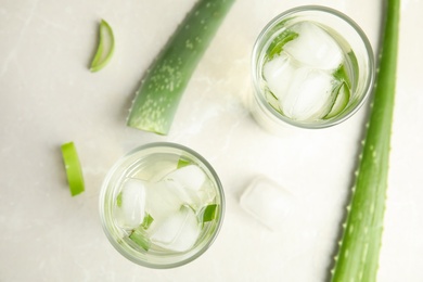 Photo of Fresh aloe drink in glasses and leaves on light table, flat lay