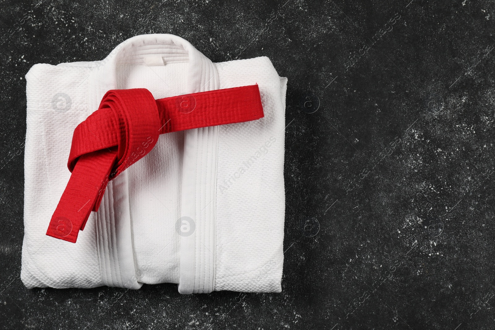 Photo of Red karate belt and white kimono on gray textured background, top view. Space for text