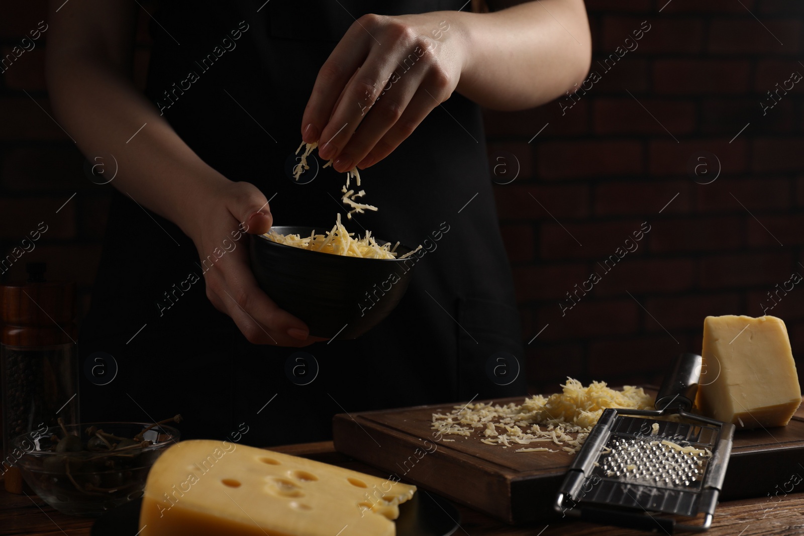 Photo of Woman with grated cheese at wooden table, closeup