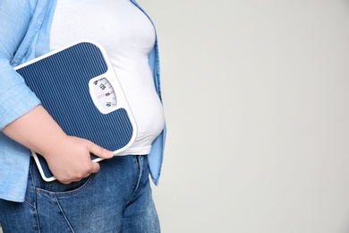 Overweight woman with scales on light background