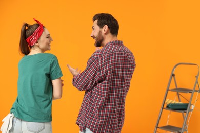 Photo of Happy designers talking near freshly painted orange wall, back view