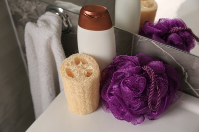Photo of Purple shower puff, loofah sponge and bottle of body wash gel on sink in bathroom