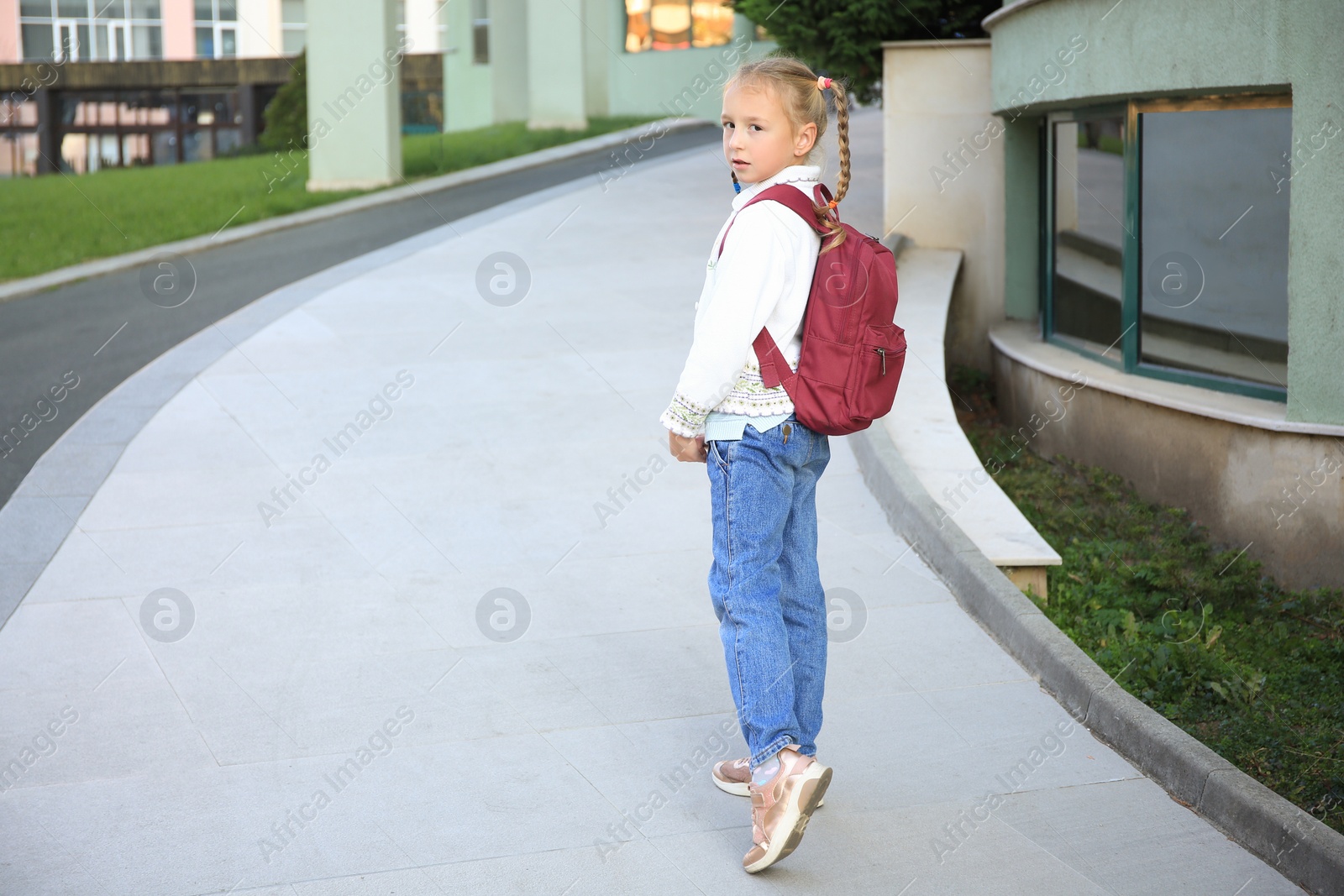 Photo of Cute little girl with backpack on city street. Space for text