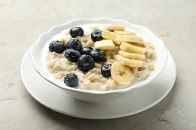 Tasty oatmeal with banana, blueberries, butter and milk served in bowl on light grey table