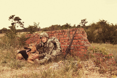 Man in military uniform with German shepherd dog near broken brick wall
