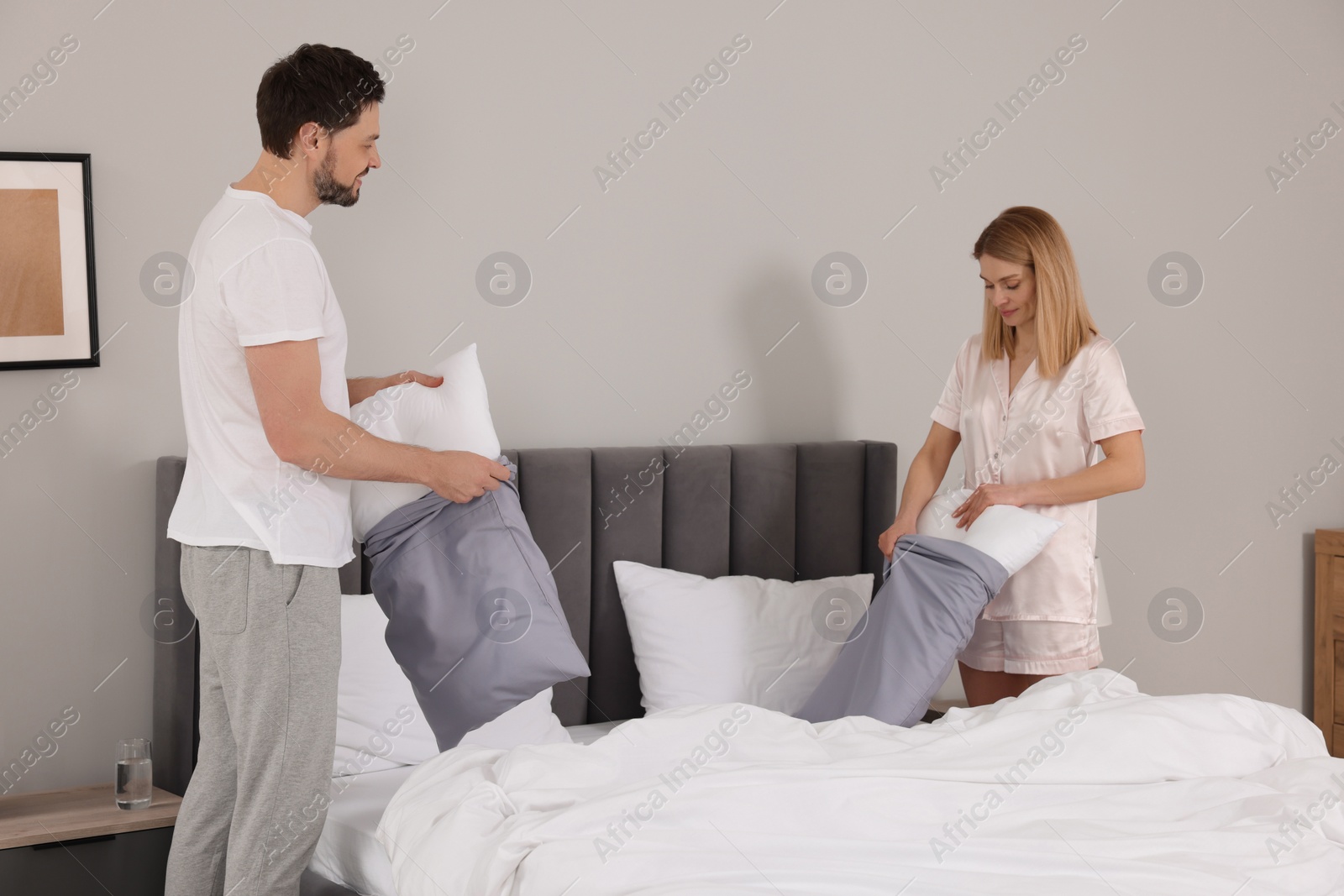 Photo of Couple changing bed linens in room. Domestic chores