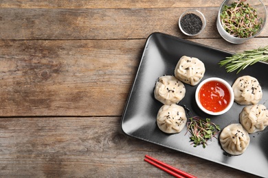 Photo of Flat lay composition with plate of tasty baozi dumplings, sprouts, sesame seeds and sauce on wooden table. Space for text