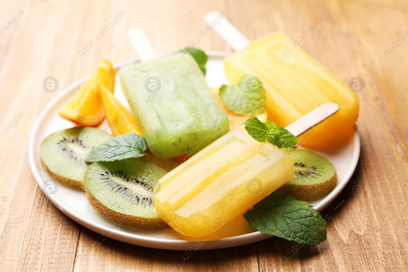 Photo of Plate of tasty orange and kiwi ice pops on wooden table. Fruit popsicle