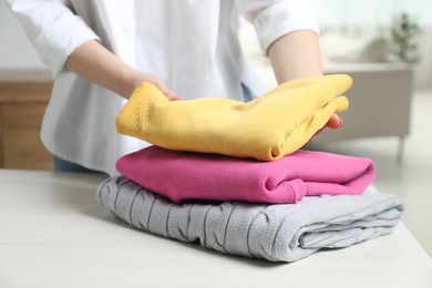 Photo of Woman folding clothes at white wooden table indoors, closeup