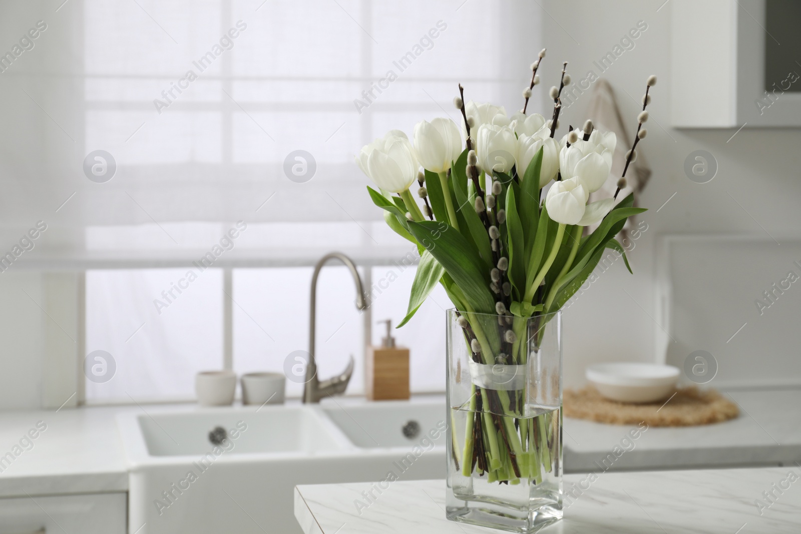 Photo of Beautiful bouquet of willow branches and tulips in vase on white table indoors, space for text