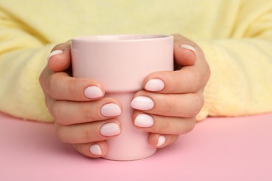 Photo of Woman with white nail polish holding cup at pink table, closeup