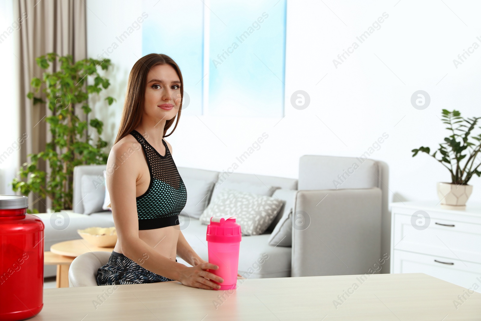 Photo of Young woman with bottle of protein shake at home. Space for text