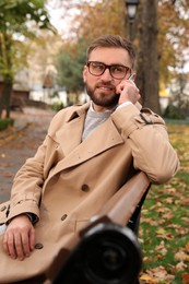 Photo of Handsome man in stylish clothes with mobile phone on bench outdoors