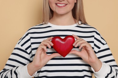 Happy volunteer holding red heart with hands on beige background, closeup