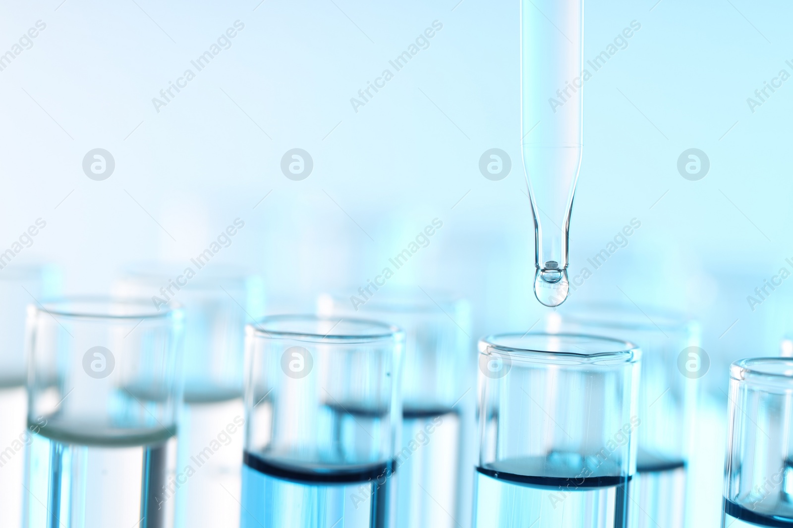 Photo of Dripping liquid from pipette into test tube on light blue background, closeup