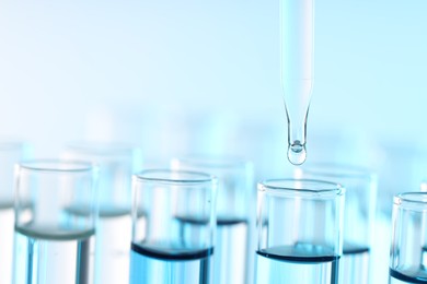 Dripping liquid from pipette into test tube on light blue background, closeup