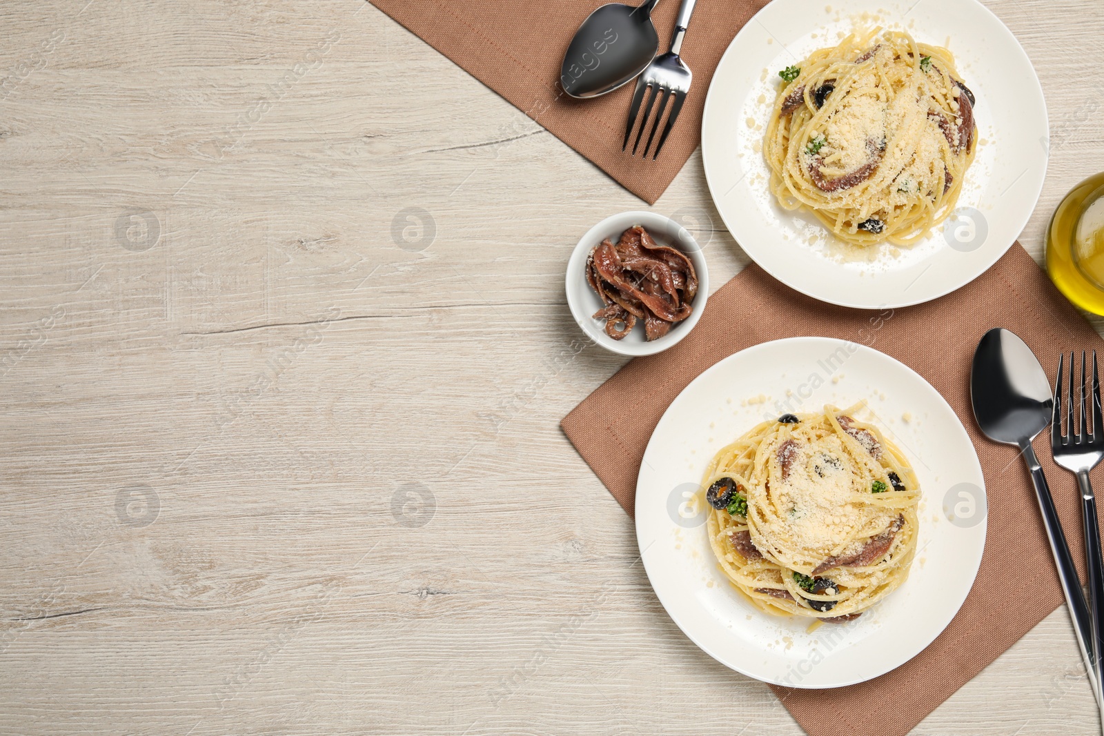 Photo of Delicious pasta with anchovies, olives and parmesan cheese served on light wooden table, flat lay. Space for text