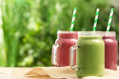 Different delicious smoothies in mason jars on wooden table against blurred background, space for text