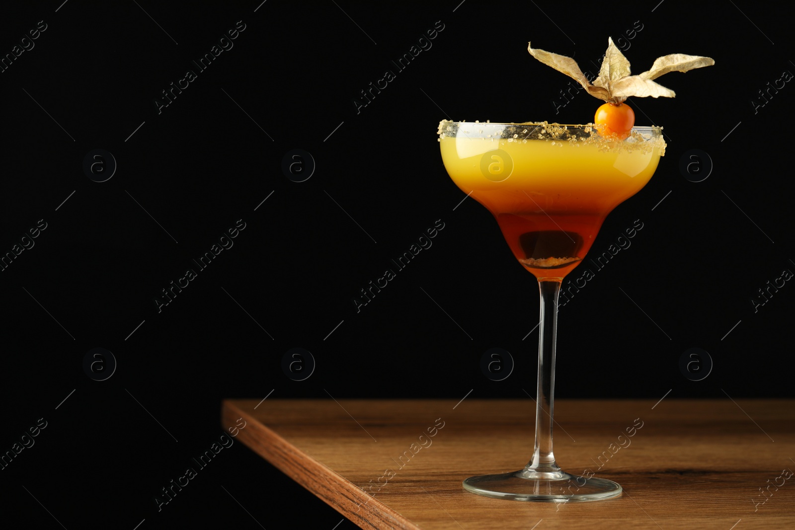 Photo of Refreshing cocktail decorated with physalis fruit on wooden table against black background. Space for text