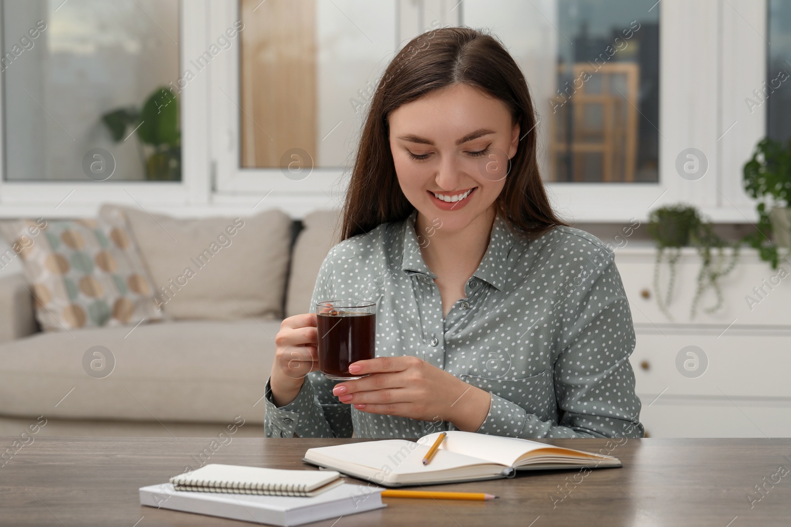 Photo of Woman with cup of coffee and notebook at wooden table indoors