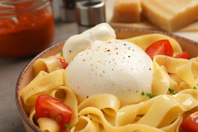 Photo of Bowl of delicious pasta with burrata and tomatoes on grey table, closeup
