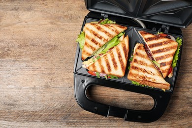 Modern grill maker with sandwiches on wooden table, top view. Space for text