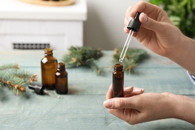 Photo of Woman dripping essential oil into glass bottle  at table, closeup