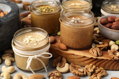 Photo of Tasty nut butters in jars and raw nuts on light grey table