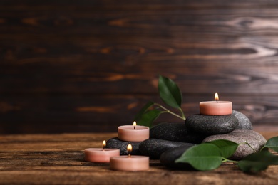 Composition of spa stones, green leaves and burning candles on wooden table, space for text