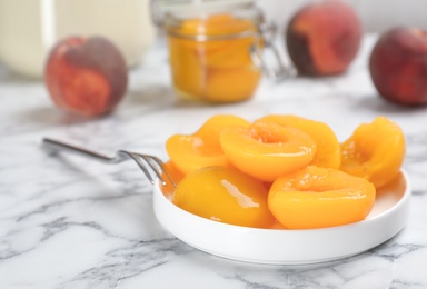 Photo of Plate with conserved peach halves on marble table